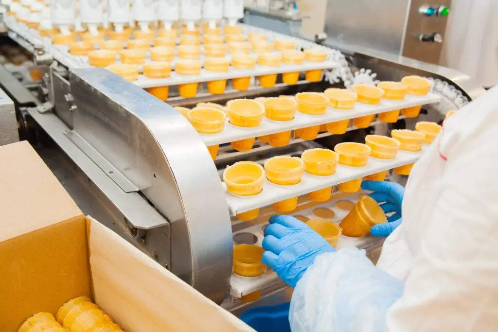 Food Assembly worker handling ice cream cones on machine line demonstrating physical hazard controls in place.