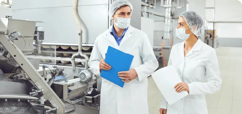 2 food production workers wearing safety outfits documenting facility.