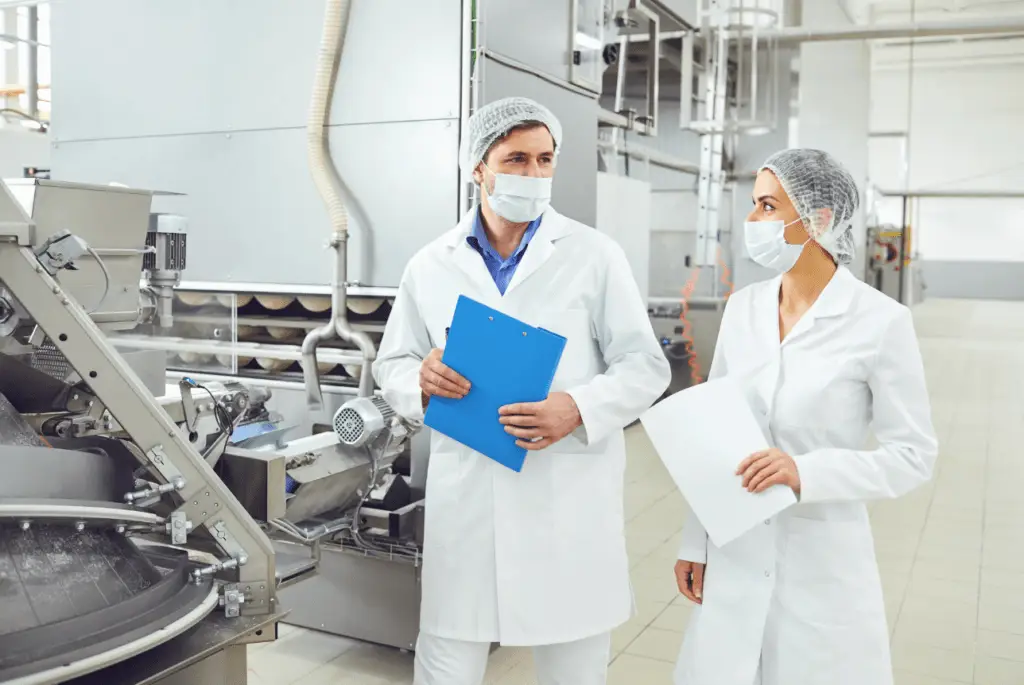 Two food production workers wearing safety outfits documenting facility.