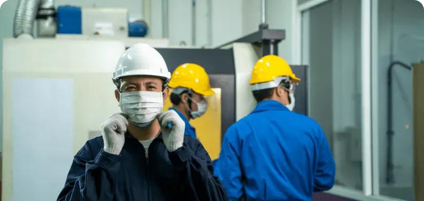 Production facility with three workers adjusting face masks with their Personal Protective Equipment, safety glasses, and hardhats.