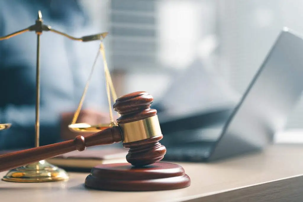 Gavel and laptop with blurred person background.