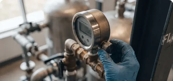 A worker wearing a blue glove adjusting a digital pressure gauge on industrial equipment.